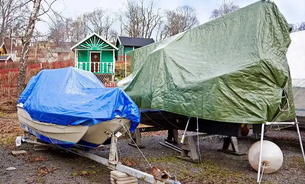 Vi ser båtar upplagda på land under presenningar.