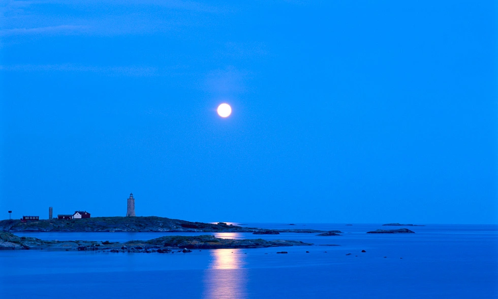 En måne lyser över en ö med fyr