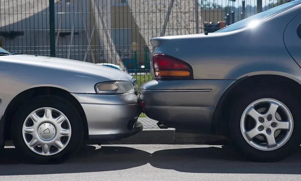 Två bilar parkerade nära varandra, nästan vidrörande vid framlyktorna, med ett staket i bakgrunden