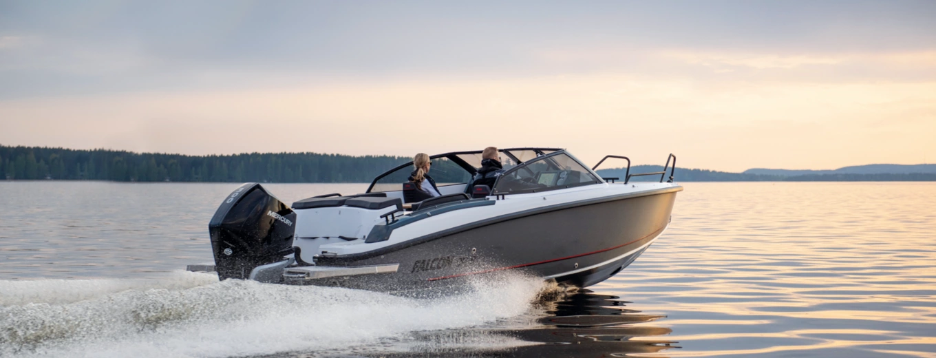 Motorbåt av märket Falcon med två personer färdas snabbt över en lugn sjö i solnedgången.