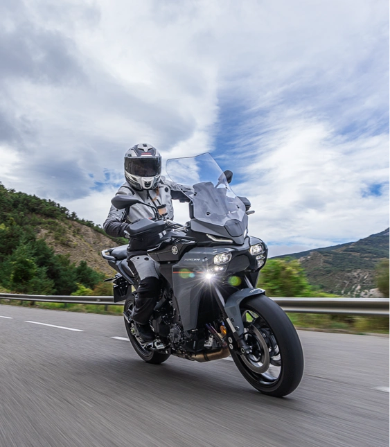 Person kör motorcykel med motorcykelutrustning på väg vid berg.