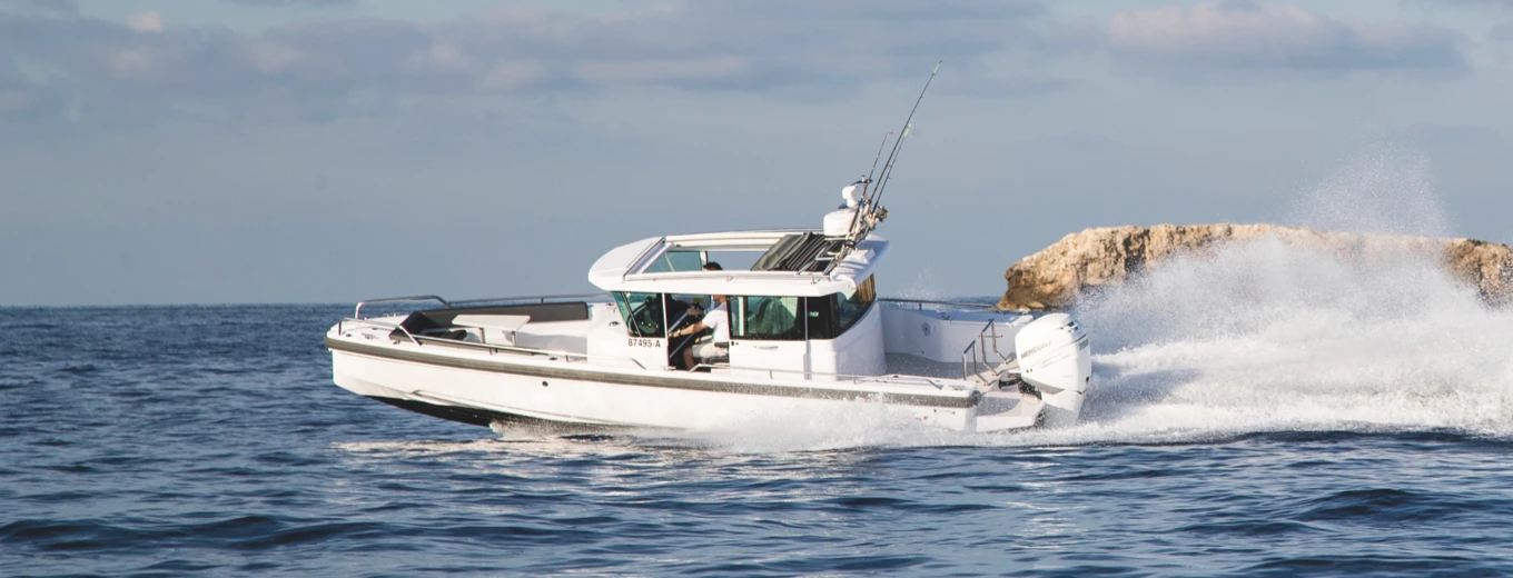 Motorbåt av märket Axopar med fiskespön på taket kör snabbt nära en klippa på öppet vatten.