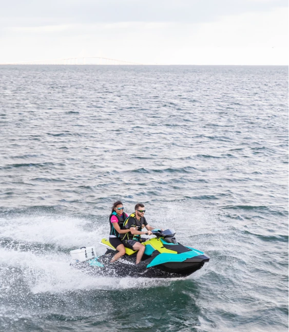 Två personer kör en färgglad vattenskoter av märket Sea-Doo på vågigt vatten.
