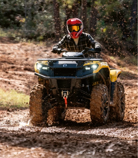 Förare med röd hjälm kör gul ATV från Can-Am genom lerig terräng.