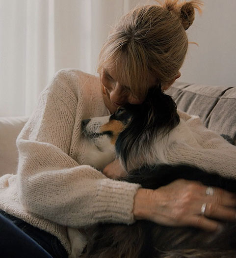Kvinna sitter i soffa och kramar sin hund.