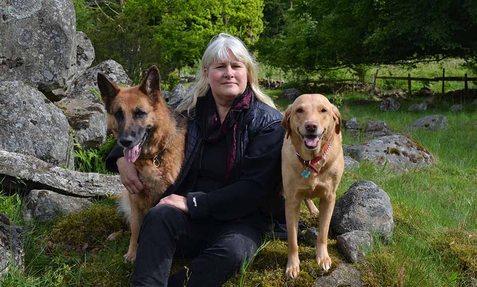 Kvinna sitter med schäfer och labrador i natur