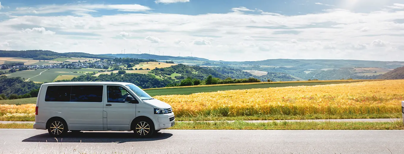 En silvergrå minivan parkerad vid sidan av en landsväg med ett gyllene fält och kullar i bakgrunden