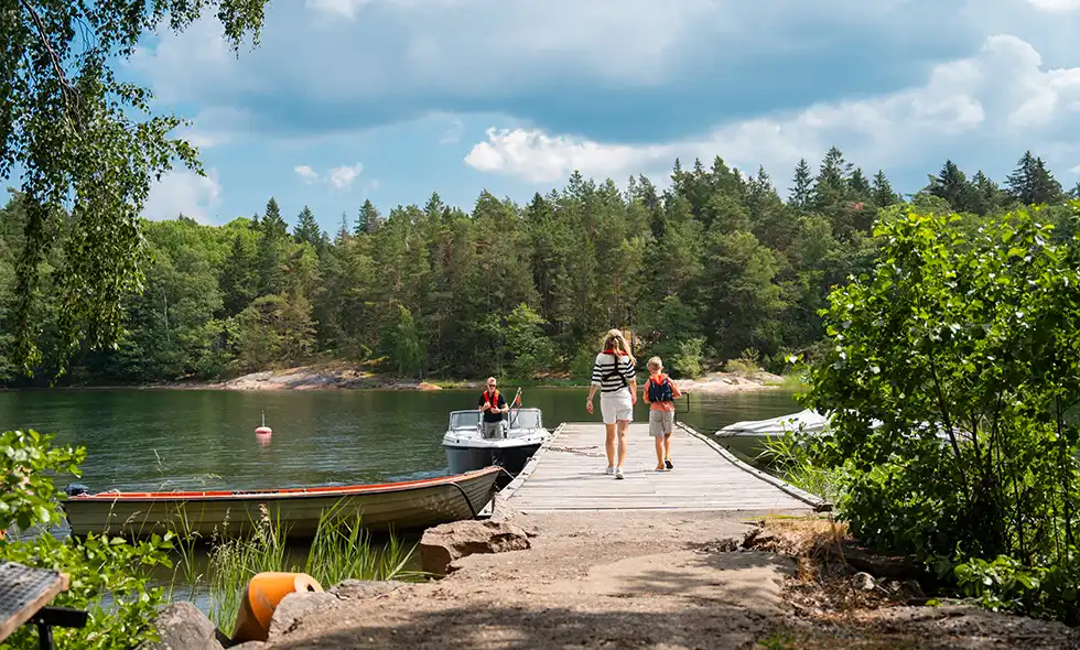 Familj med båt som är på en brygga i sommarnatur.