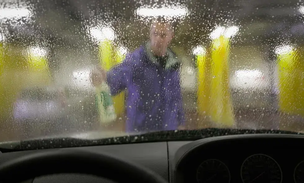 En person i blå kläder tvättar framrutan på en bil