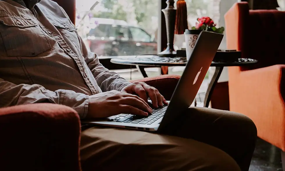 En man sitter på ett café och jobbar på sin dator.