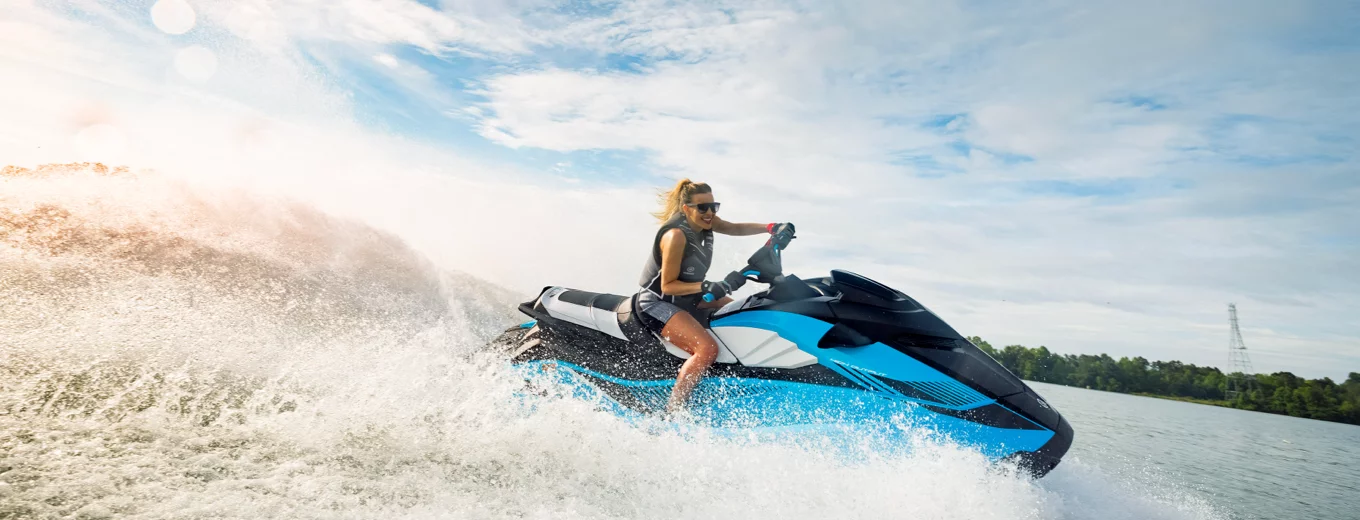 Kvinna kör en blå vattenskoter av märket Yamaha snabbt på vattnet med vattenstänk och vågor runtomkring.