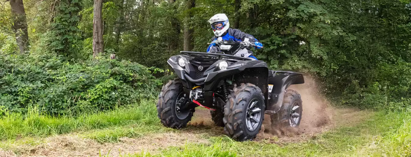 Förare i blå jacka kör svart ATV från Yamaha på skogsstig.