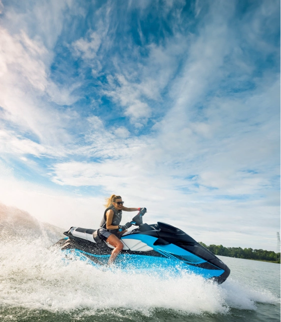 Kvinna kör en blå vattenskoter av märket Yamaha snabbt på vattnet med vattenstänk och vågor runtomkring.