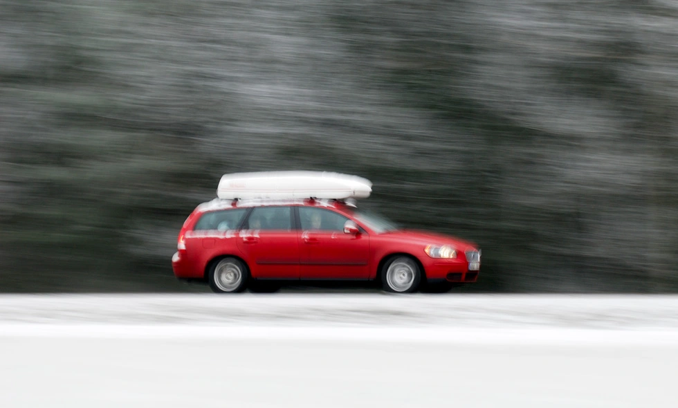 En röd bil med takbox kör på en snöig väg