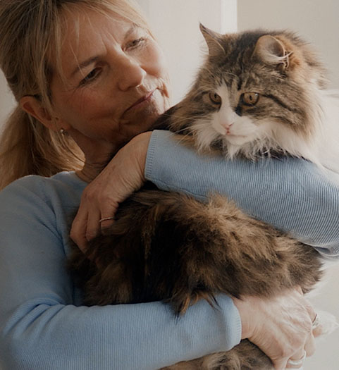 En kvinna håller en stor långhårig katt kärleksfullt i sina armar