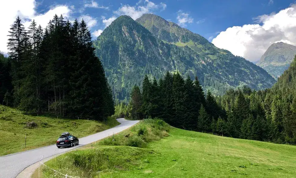 En bil kör på en väg omgiven av berg och skog