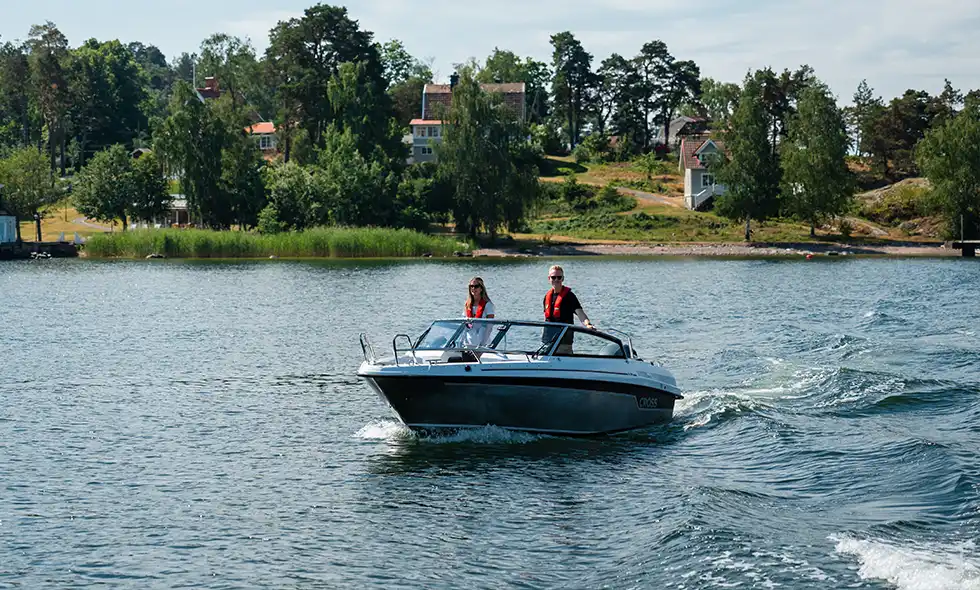 Två människor på en båt i solen med natur i bakgrunden. 