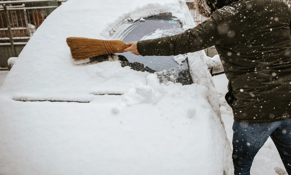 En person borstar bort snö från en bil under en snöig dag.