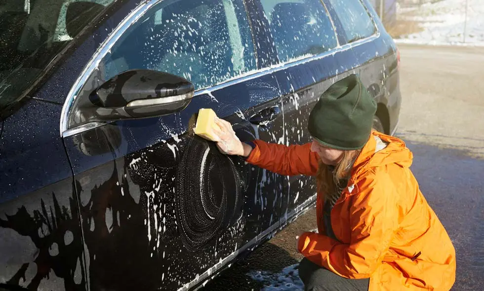 En person i orange jacka tvättar en svart bil