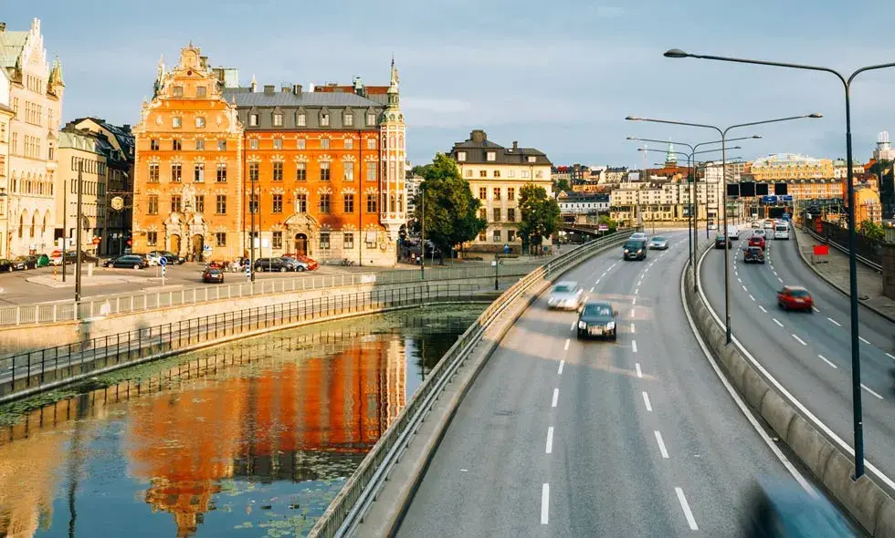 Stadssiluett på Stockholm stad med historiska byggnader vid floden och en trafikerad väg i förgrunden