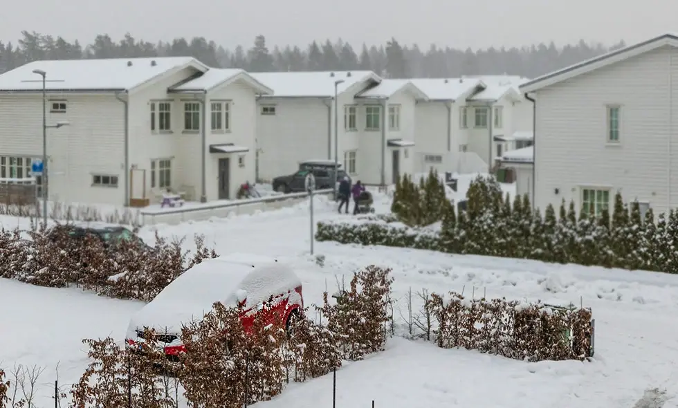 En parkerad bil täckt med snö framför radhus i ett bostadsområde